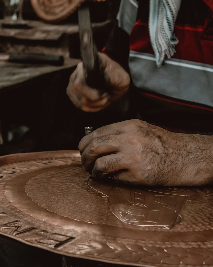Detalle de un cincel y un martillo definiendo un motivo grabado sobre una plancha metálica