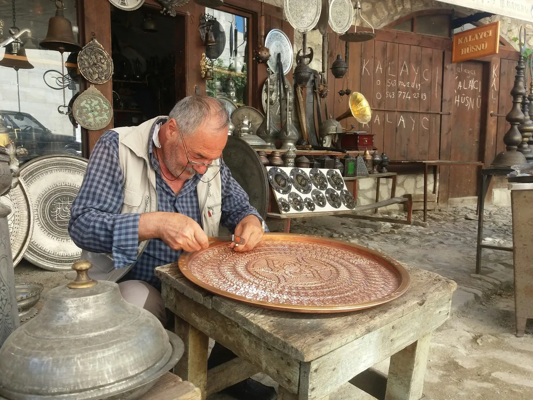 Artesano trabajando un motivo en relieve sobre una bandeja de cobre con cincel y martillo